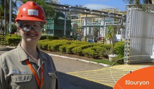 Mulher de capacete laranja em frente de indústria