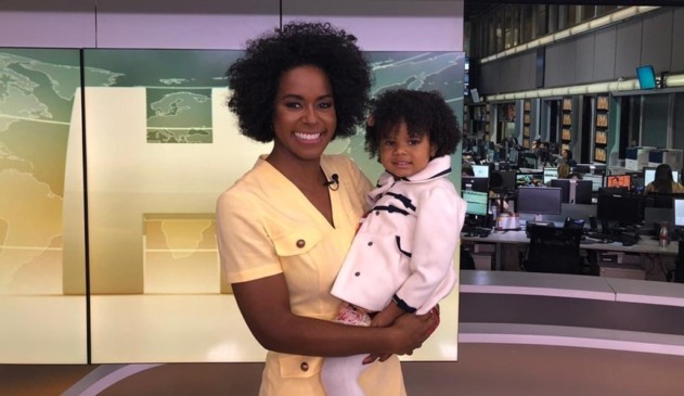 Maju Coutinho, com vestido amarelo, segurando criança negra com roupa branca