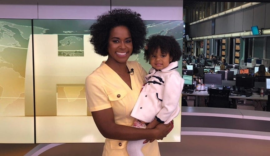 Maju Coutinho, com vestido amarelo, segurando criança negra com roupa branca