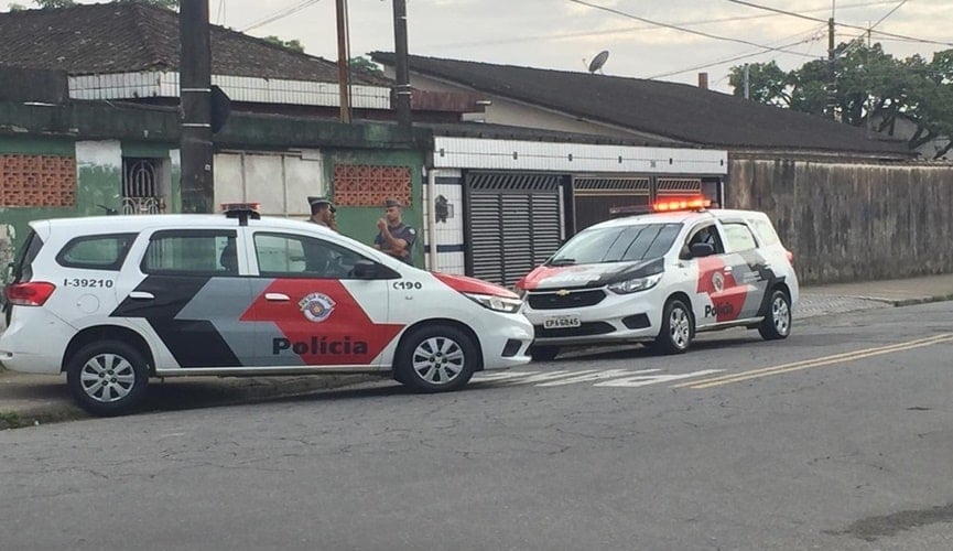 Policiais na frente de residência ao lado de viaturas da Polícia Militar