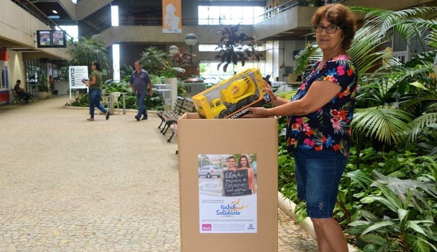 Senhora depositando caminhão de brinquedo em caixa de papelão