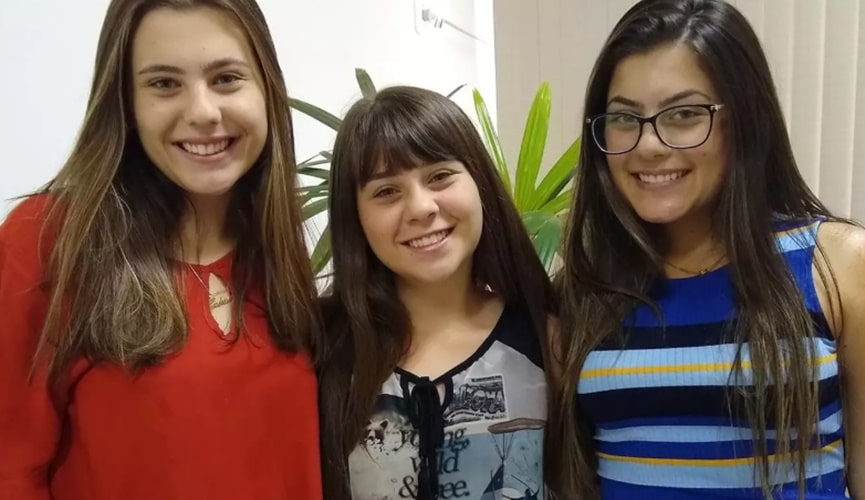 Mulher de blusa de manga longa vermelha, à esquerda; mulher de franja com blusa mesclada nas cores preta, branca e cinza, ao centro; mulher de óculos com blusa listrada nos tons de azul claro e escuro, rosa e preto.