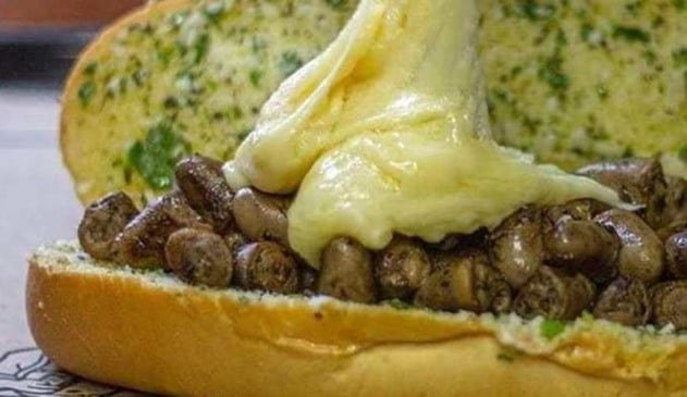 Foto de lanche feito de pão de alho, com recheio de coração de frango e coberto por queijo derretido.