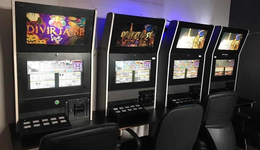 Quatro máquinas caça-níquel em fileiras, com telas de jogos abertas.