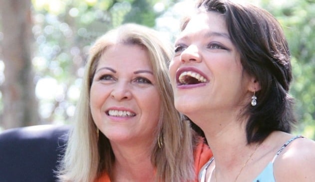 Jovem de cabelos escuros sorrindo ao lado de mulher loira