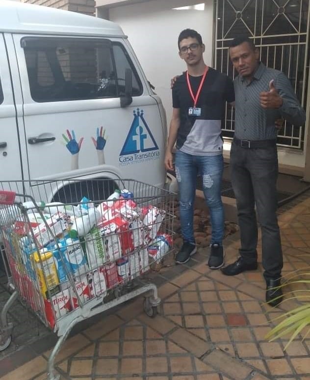 Homem negro de roupa social ao lado de rapaz jovem de barba com carrinho de compras com leites
