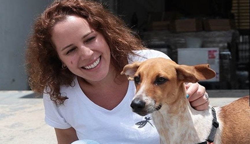 Mulher vestindo camiseta branca abraçada com cachorro amarelo e branco.