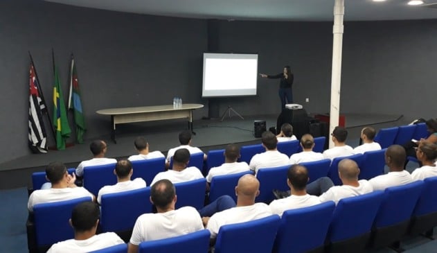 Guardas municipais assistindo palestra ministrada por mulher de cabelos longos e roupa preta