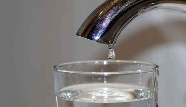 Torneira da cor prata gotejando água em um copo de água