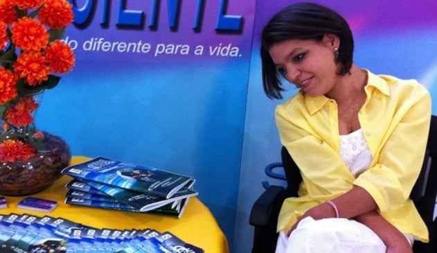 Mulher cadeirante ao lado de mesa com revistas e flores