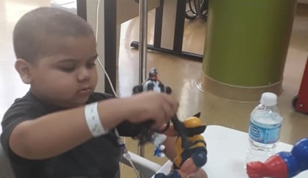 Garoto careca com camiseta preta brincando com bonecos em um ambiente hospitalar