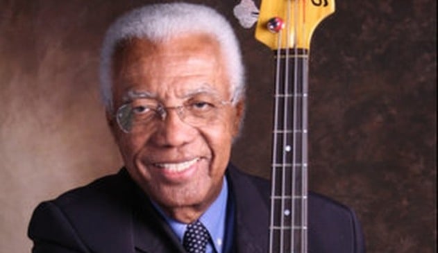 Homem negro de óculos, sorrindo com baixo em mãos