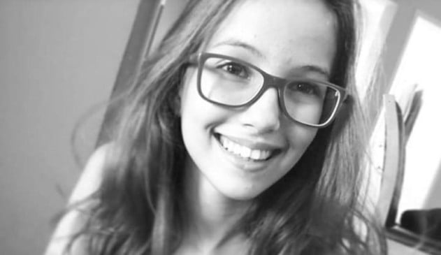 Foto preta e branca de menina de cabelos longos, com óculos, sorrindo