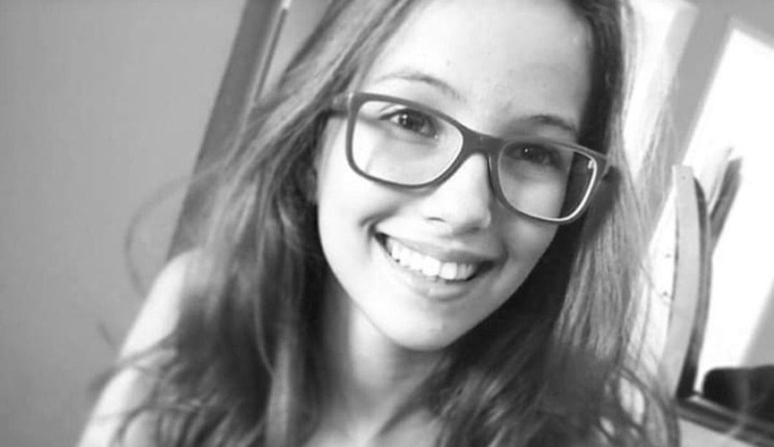 Foto preta e branca de menina de cabelos longos, com óculos, sorrindo