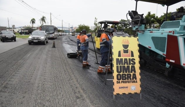 Operários e máquinas colocando asfalto em via