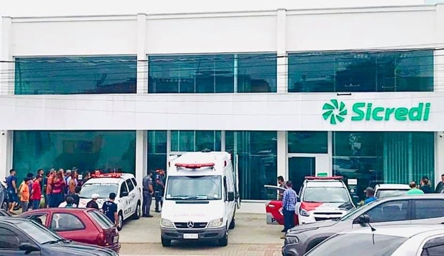 Foto da entrada do Sicredi com ambulância, policiais civis e militares
