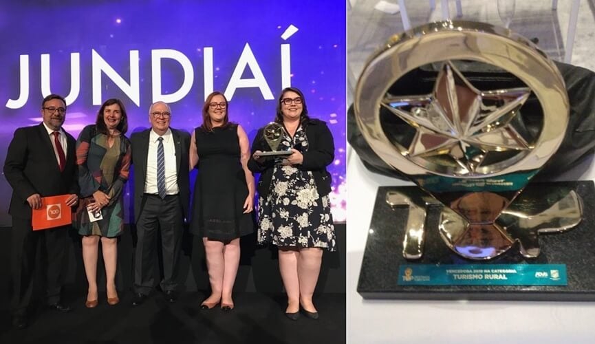 Grupo de pessoas formado por três mulheres e dois homens, com roupas de gala, à esquerda; à direita, prêmio de turismo rural