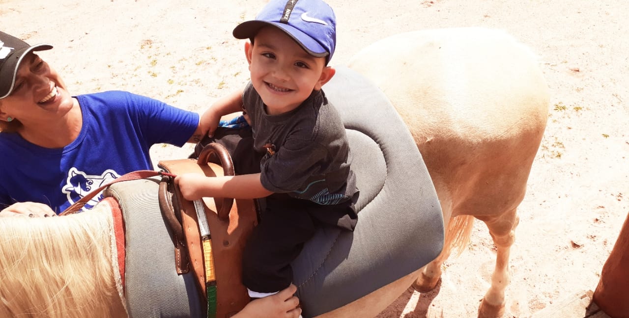 Criança andando de cavalo, acompanhada de mulher adulta