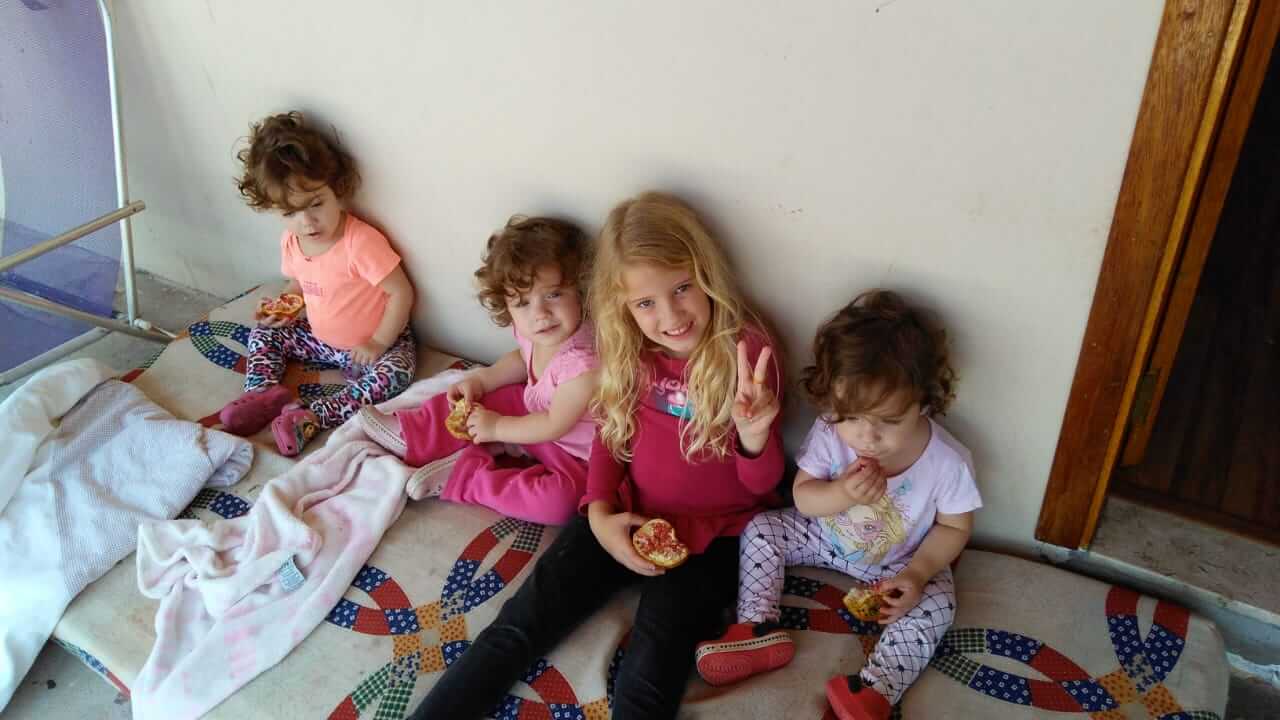 Quatro meninas sentadas em colchão comendo torrada