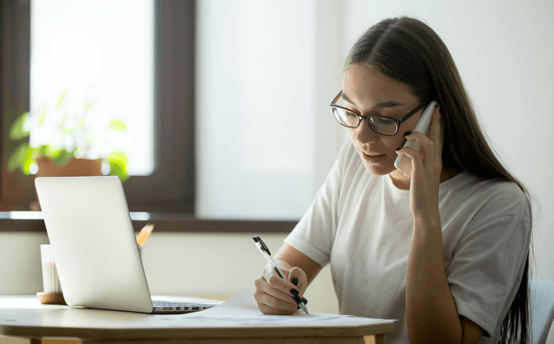 Mulher fala ao celular com notebook aberto à frente
