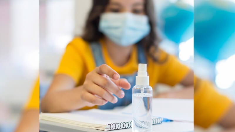 Criança em sala de aula com máscara e álcool em gel