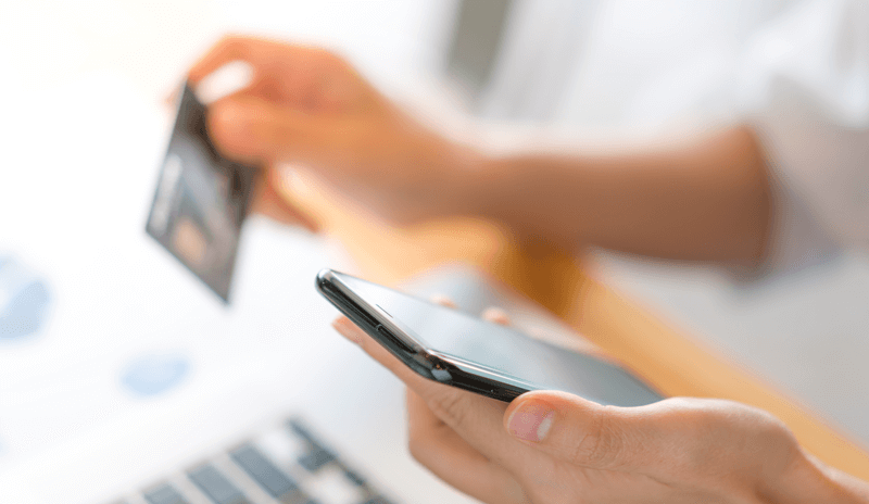 Pessoa usa cartão de crédito e celular para realizar compra