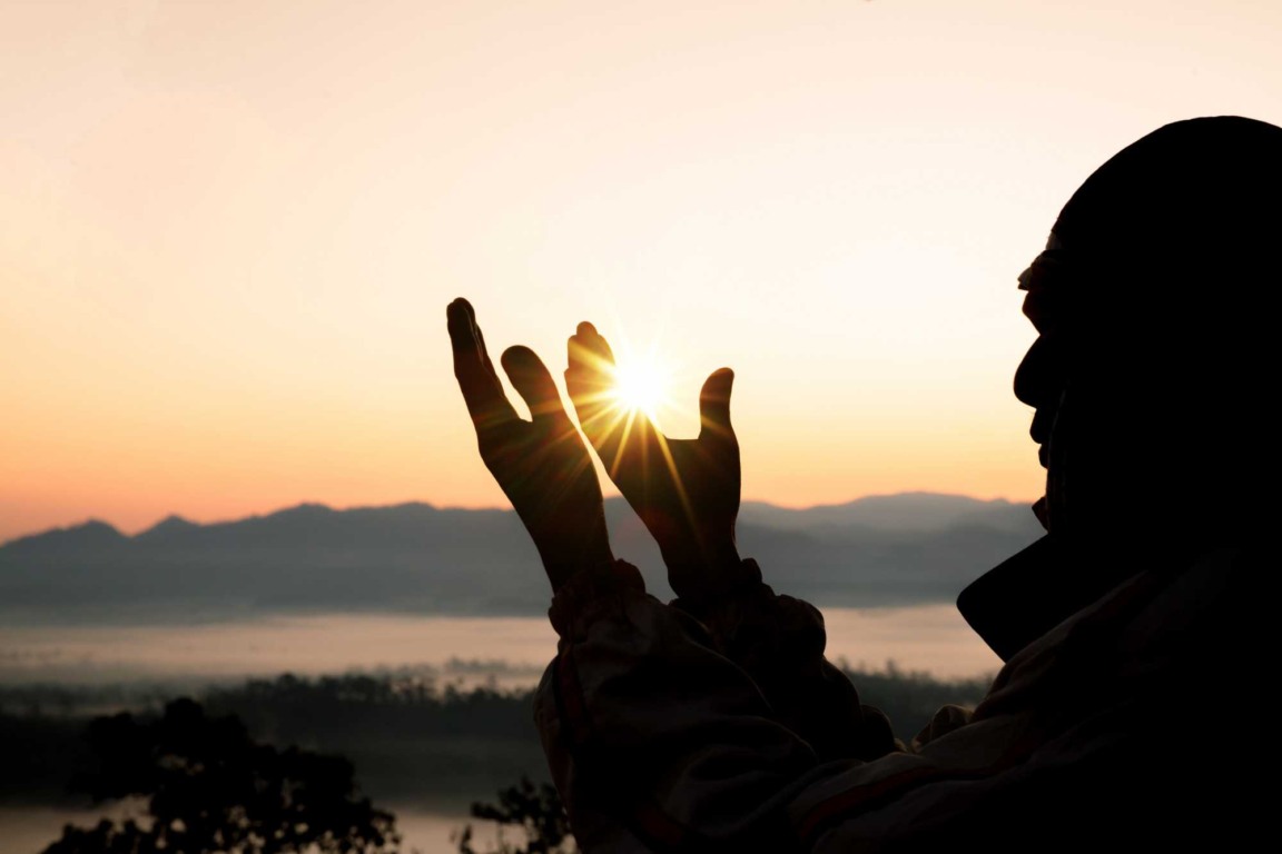 Pai de Santo em silhueta, segurando o sol com as mãos durante o nascer do sol, com montanhas ao fundo. Pai de Santo em silhueta, segurando o sol com as mãos durante o nascer do sol, com montanhas ao fundo.