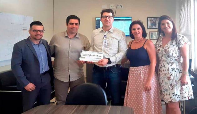 Superintendente do Hospital São Vicente ao meio recebendo cheque simbólico das mãos do presidente da ACE Jundiaíi, ao seu lado esquerdo. também há um outro homem e duas outras mulheres na foto, da diretoria da ACE