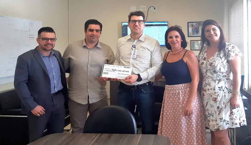 Superintendente do Hospital São Vicente ao meio recebendo cheque simbólico das mãos do presidente da ACE Jundiaíi, ao seu lado esquerdo. também há um outro homem e duas outras mulheres na foto, da diretoria da ACE