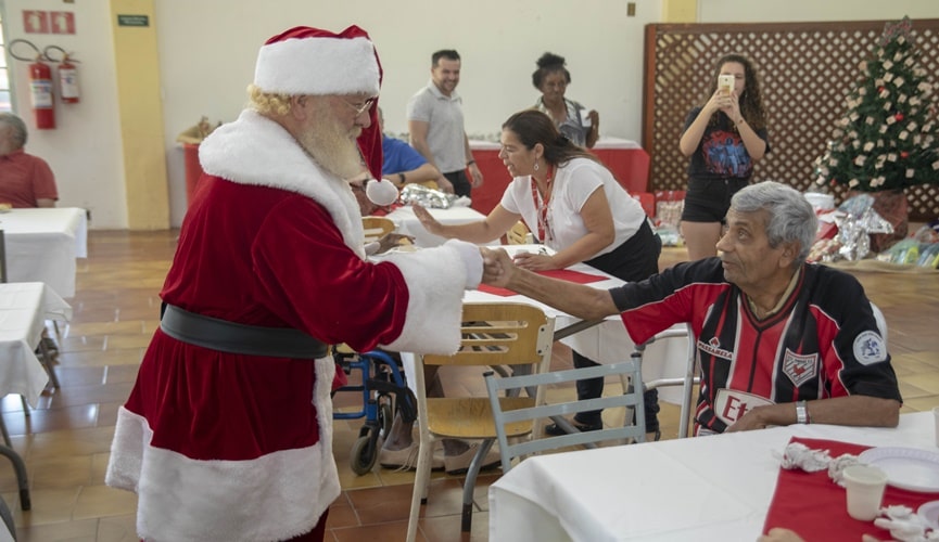 Papai Noel apertando mão de idoso