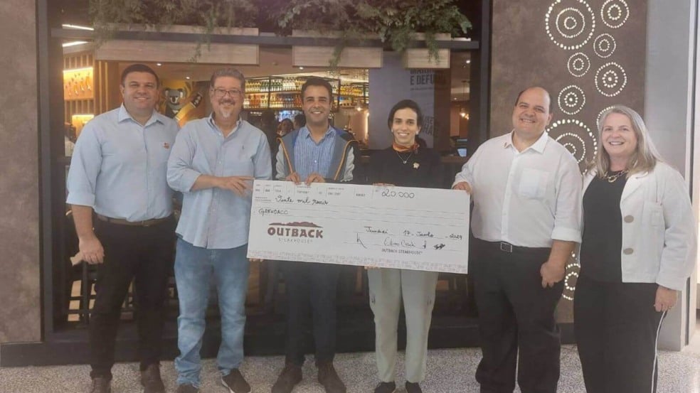 Pessoas segurando um cheque representando R$ 20 mil em gift cards do Outback do Maxi Shopping Jundiaí para o Grendacc