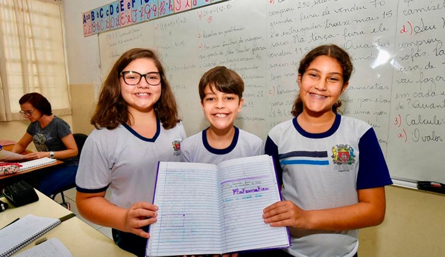 Três alunos seguram caderno com conteúdos de matemática