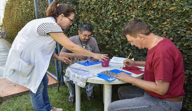 Dois homens em mesa rdonda confecionam agendas enquanto são orientados por mulher