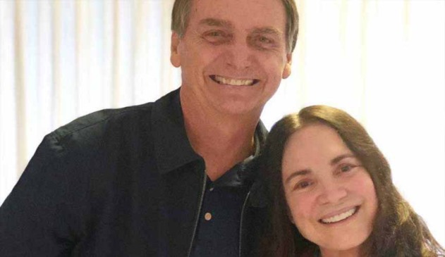 O presidente Jair Bolsonaro posa ao lado da atriz Regina Duarte. Ambos sorriem na foto.