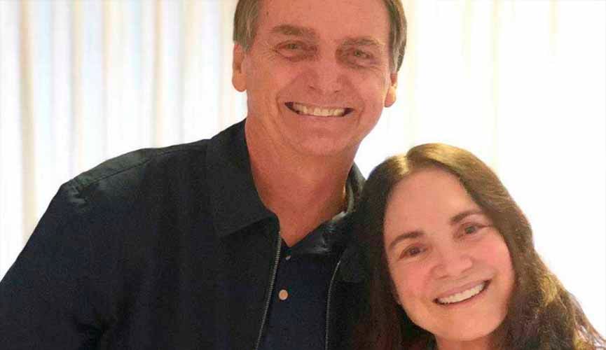 O presidente Jair Bolsonaro posa ao lado da atriz Regina Duarte. Ambos sorriem na foto.
