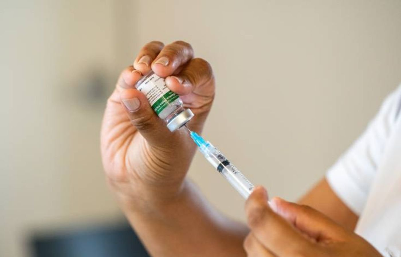 Profissional de saúde retira dose da vacina da gripe com uma seringa, utilizando frasco do Instituto Butantan em ambiente clínico.