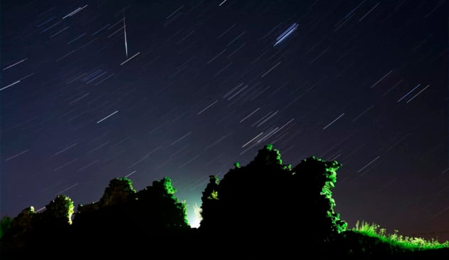 Foto tirada com longa exposição mostra um meteoro Perseid cruzando o céu na vertical e o rastro das estrelas acima das ruínas de um castelo medieval na vila de Kreva, a cerca de 100 km a noroeste de Minsk, na Bielorrússia
