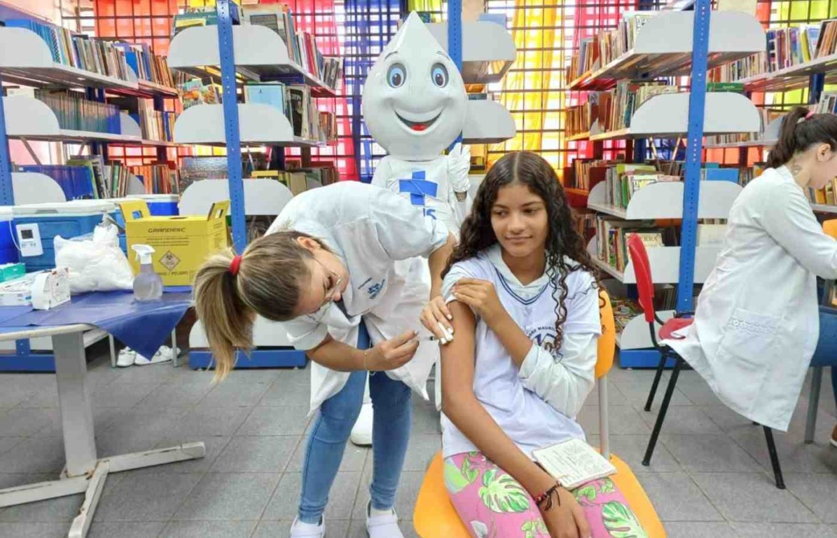 Estudante recebe vacina em escola durante ação de cobertura vacinal em Jundiaí, com presença do personagem Zé Gotinha.