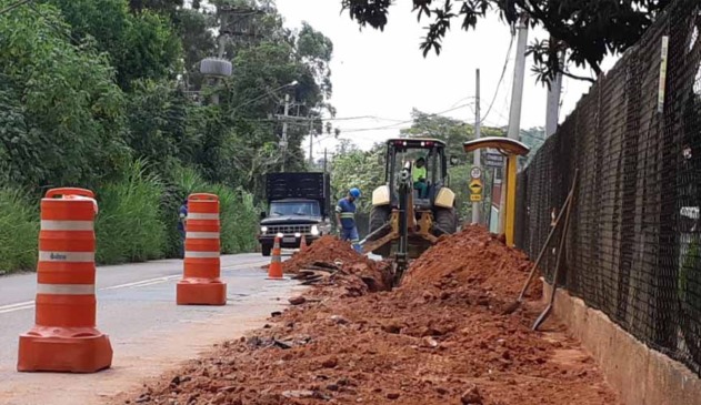 obra em avenida, com cones ao lado esquerdo onde há asfalto e, no meio fio e na calçada, terra por conta da obra de rede de água.