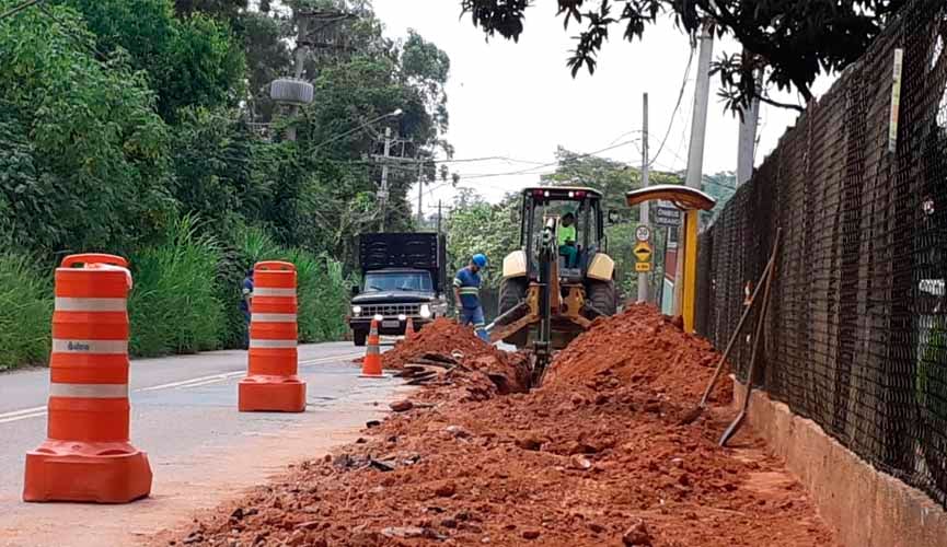 obra em avenida, com cones ao lado esquerdo onde há asfalto e, no meio fio e na calçada, terra por conta da obra de rede de água.