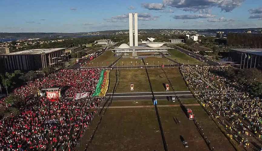 cena do documentário democracia em vertigem, onde um paredão separa manifestantes em frente ao congresso nacional. à esquerda, manifestantes de vermelho e de esquerda; à direita, manifestantes de direita.