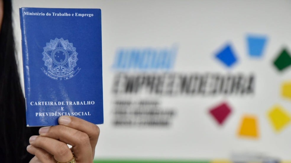 Carteira de trabalho sendo segurada à frente de parede da sede do Programa Jundiaí Empreendedora.