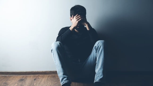 Homem sentado sozinho em chão de casa.