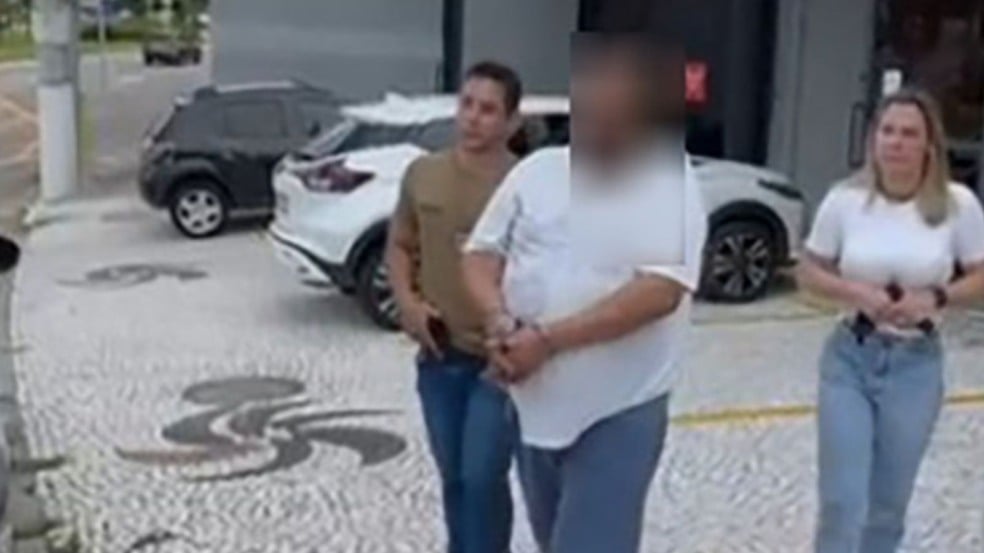 Homem algemado ao lado de policiais.