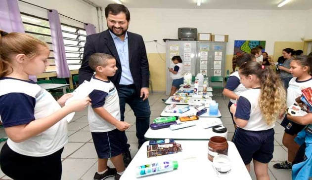 prefeito de jundiaí com alunos, enquanto os mesmos expoem, em mesa dentro da sala de aula, embalagens de produtos dentro de projeto de educação financeira