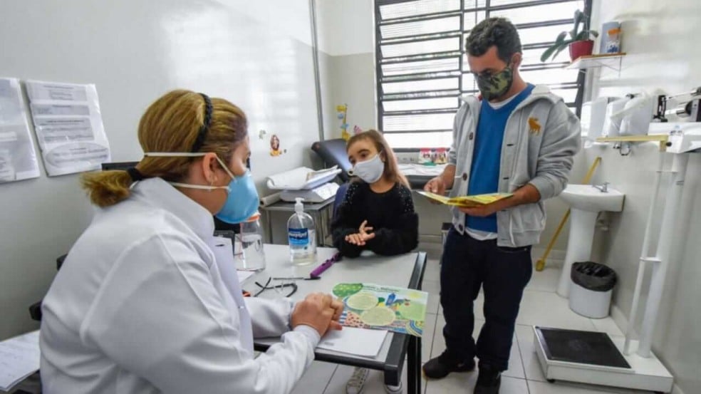 Criança em consulta médica com o pai e pediatra em consultório de UBS em Jundiaí