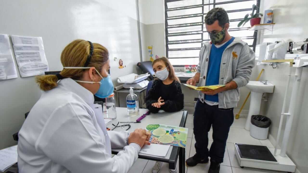 Criança em consulta médica com o pai e pediatra em consultório de UBS em Jundiaí