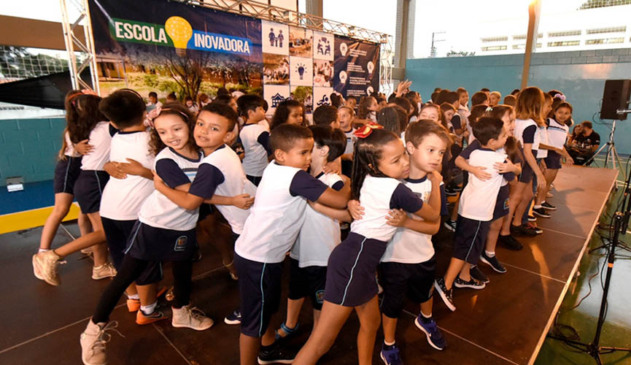 crianças fazem apresentação musical durante a entrega do espaço como Escola Inovadora. Eles estão de uniforme escola, em palco montado na quadra