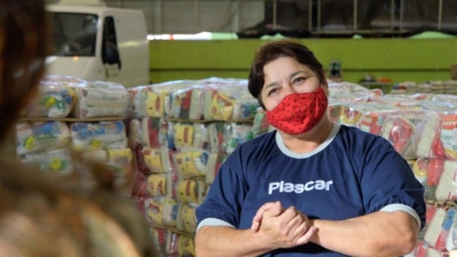 Mulher com uniforme da Plascar, em frente à doações de cestas básicas