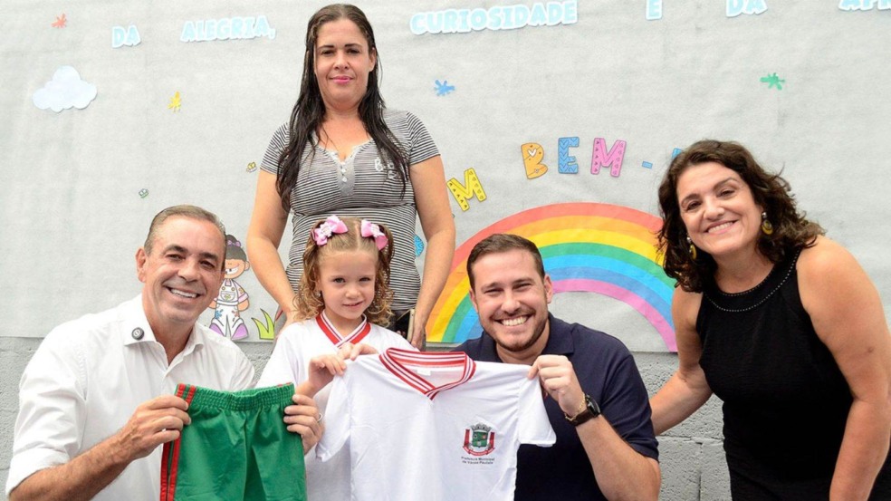 Prefeito prof. Rodolfo Braga, vice João Paulo e criança recebendo uniforme